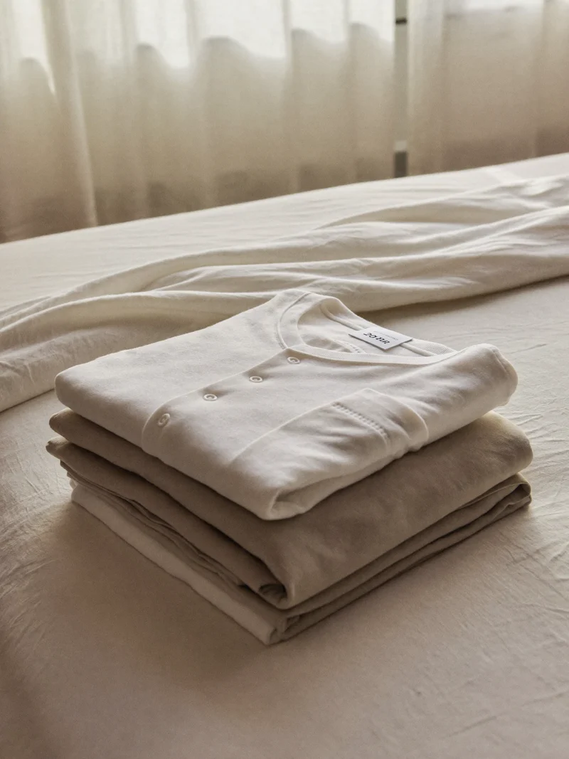 Pijamale din jerseu de bumbac, împăturite pe un pat de copil cu lenjerie simplă.